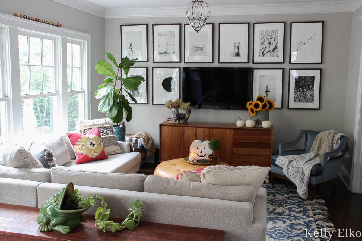 Beautiful gallery wall helps the tv blend into the background and I love all the black and white photography kellyelko.com #gallerywall #blackandwhite #photography #minted #tvgallerywall #familyroomdecor #eclecticdecor #sectionalsofa #houseplants #cozydecor #colorfuldecor