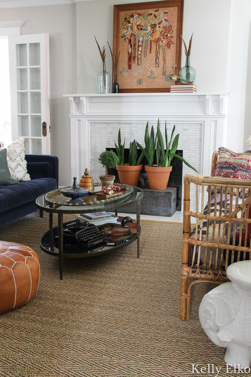 Love this eclectic living room with vintage crewel art and other unique pieces kellyelko.com #fall #falldecor #eclecticdecor #uniquedecor #livingroom #livingroomdecor #fallmantel #manteldecor #vintageart #crewel #houseplants #hearth 