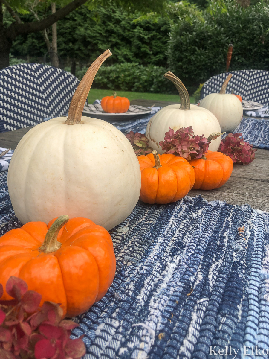 Love this simple fall centerpiece of white and orange pumpkins on blue table runners kellyelko.com #pumpkins #pumpkindecor #falldecor #fallcenterpiece #gourds #farmhousedecor #farmhousefall 