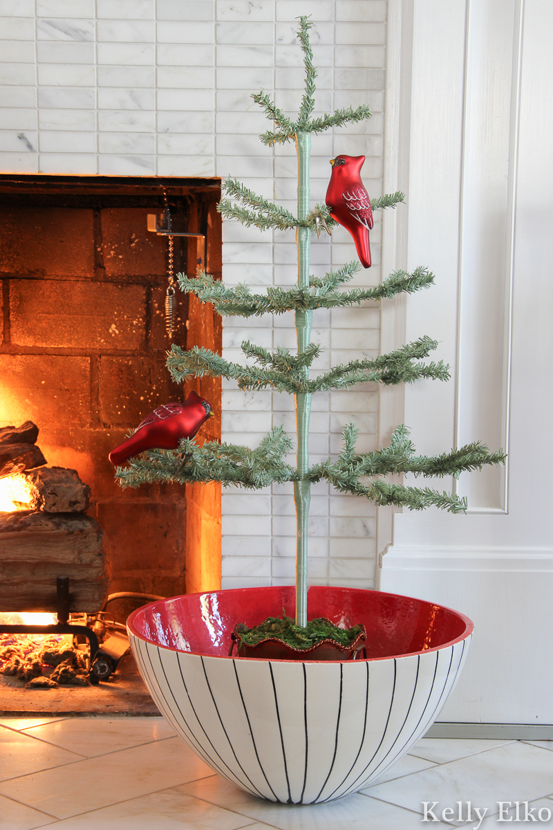 Love this little feather tree in a big red bowl kellyelko.com #feathertree #sparsetree #sparsechristmastree #vintagechristmas #retrochristmas #cardinalornament #christmasmantel