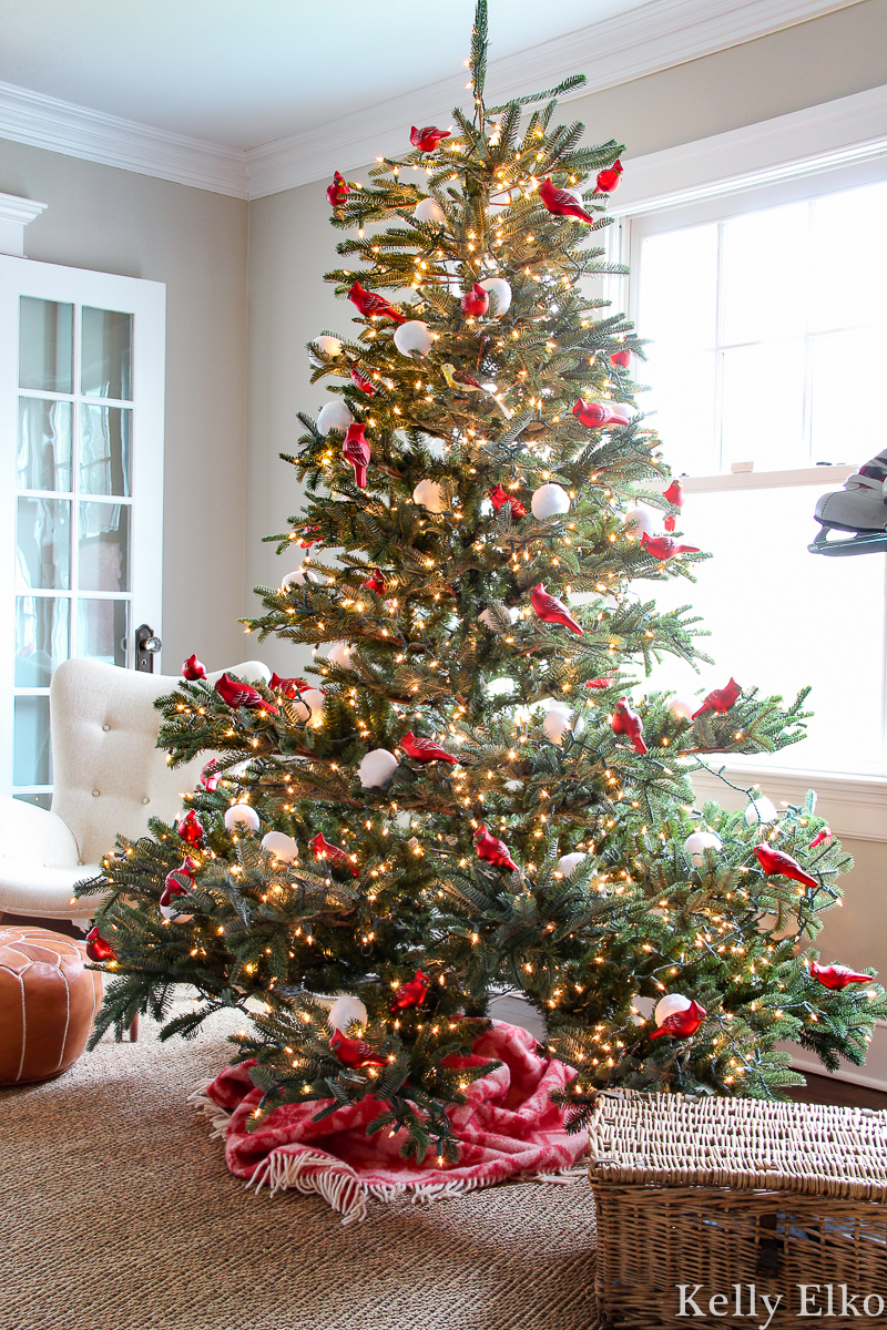 WOW love this realistic looking sparse Christmas tree filled with red carinal ornaments kellyelko.com #sparsechristmastree #realisticchristmastree #vintagechristmas #christmastree #christmasornaments #rattanfurniture #daybed #cozychristmas #farmhousechristmas #treeskirt