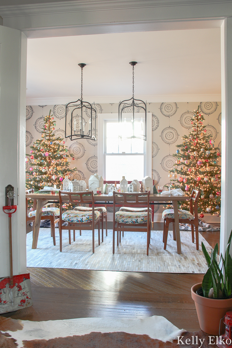 Love the pair of sparse Christmas trees in this stunning dining room kellyelko.com #christmasdecor #christmastrees #realisticchristmastree #sparsechristmastree #christmasdiningroom #farmhousechristmas 