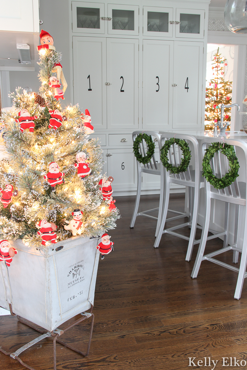 Love this festive Christmas home tour and the adorable little Christmas tree covered in vintage Santa ornaments in an old canvas laundry bin kellyelko.com #christmasdecor #christmasornaments #vintagechristmas #retrochristmas #vintagesanta #vintageornaments #vintagesantaornament #christmaskitchen #boxwoodwreaths #christmashometour #christmaswreath #vintagedecor 