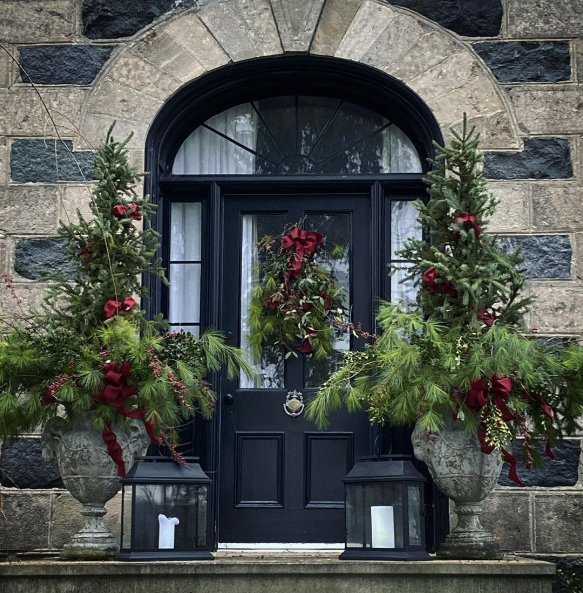 Beautiful old stone farmhouse dressed for Christmas #christmas #farmhousechristmas #christmasporch #christmasurns #christmasplanters #outdoorchristmasdecor #classicchristmas