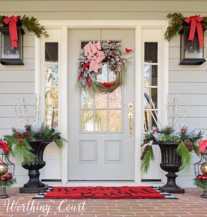 Classic red and green Christmas porch with DIY cardinal wreath #christmas #christmasporch #ourdoorchristmasdecor #diywreath #christmaswreath #farmhousechristmas #christmasurns #christmasplanters 