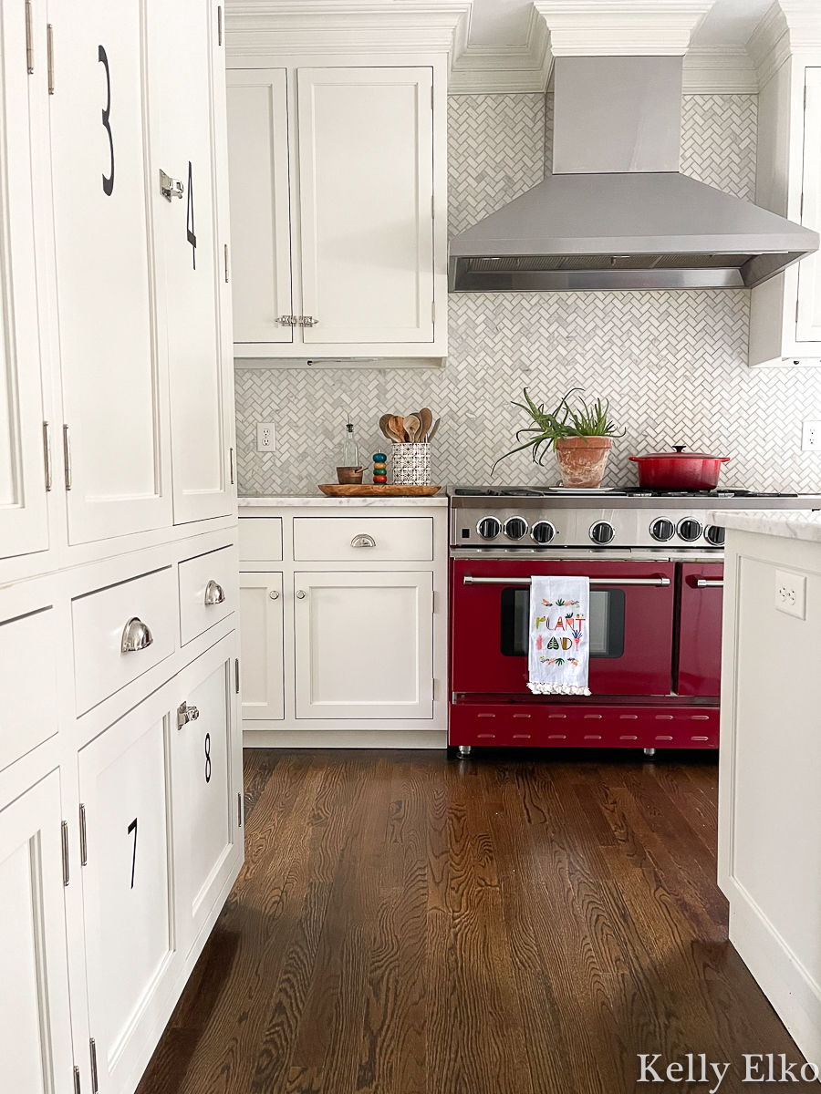 White kitchen with red stove and herringbone carrara marble backsplash kellyelko.com