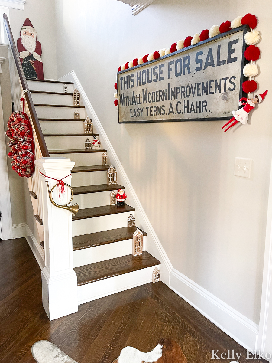 Beautiful Christmas foyer - love the wood houses on the stairs and the antique wood sign kellyelko.com