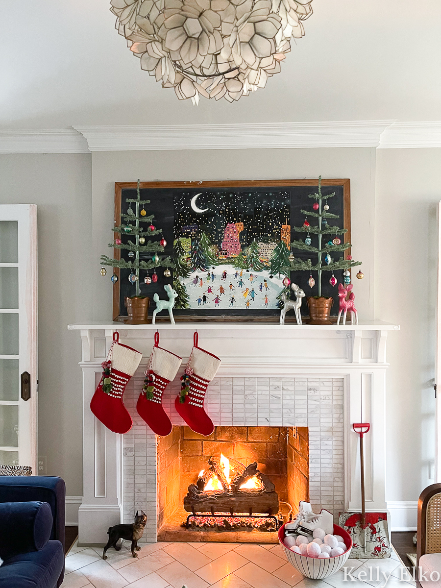 Gorgeous colorful Christmas mantel with ice skaters in NYC art, feather trees, vintage ornaments and whimsical pom pom stockings kellyelko.com