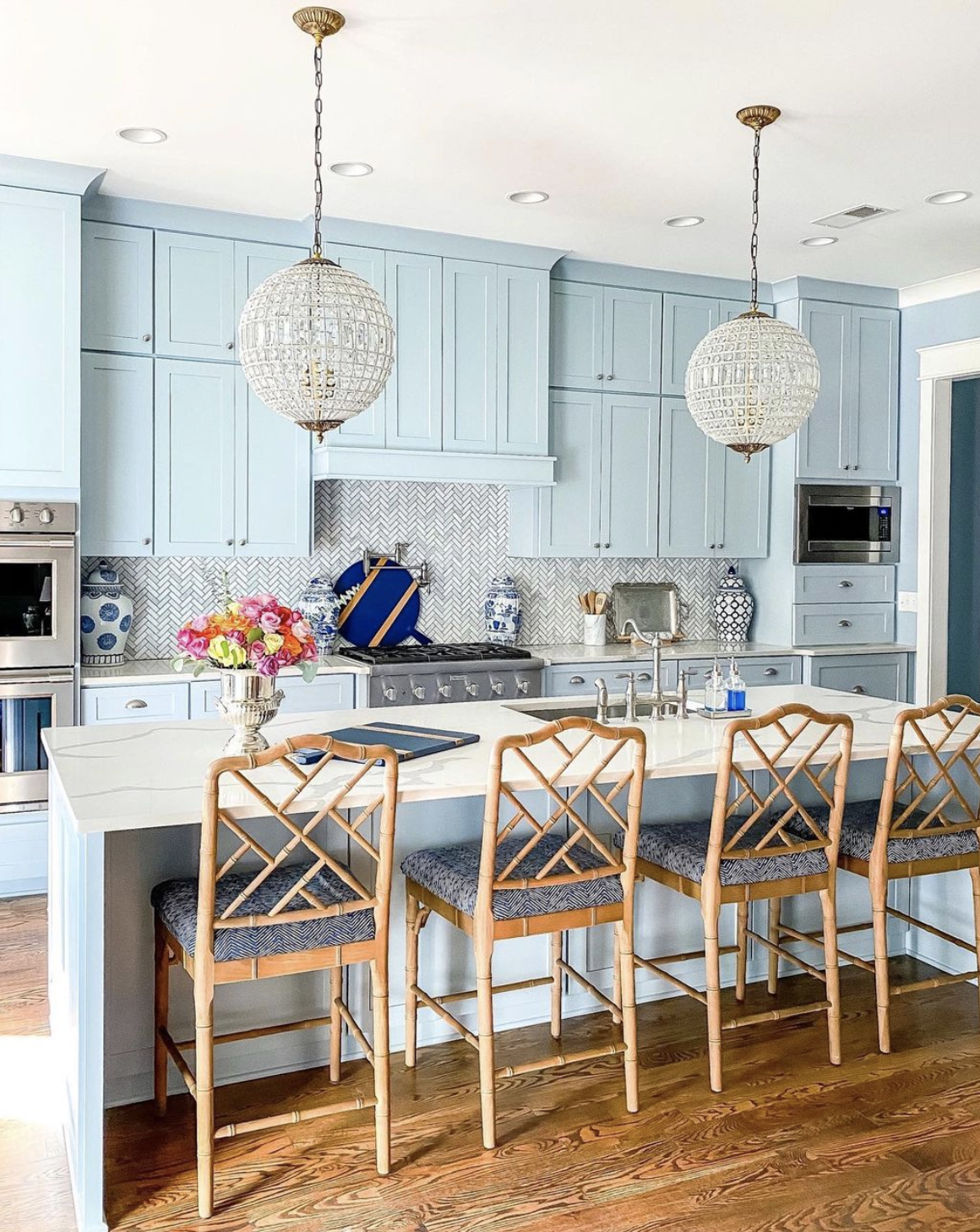 Gorgeous blue kitchen cabinets with rattan stools and brass and crystal pendant lights kellyelko.com