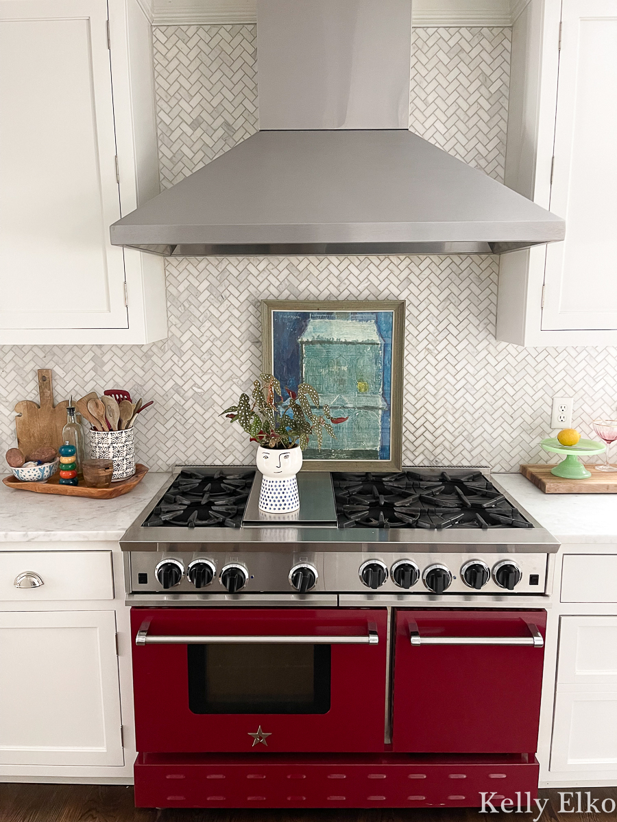 Gorgeous white kitchen with herringbone marble tile backsplash and red stove kellyelko.com